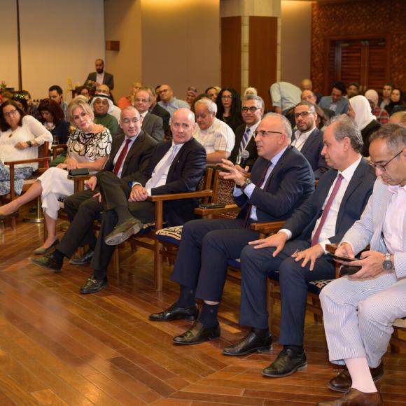 An audience of men and women are sitting on chairs