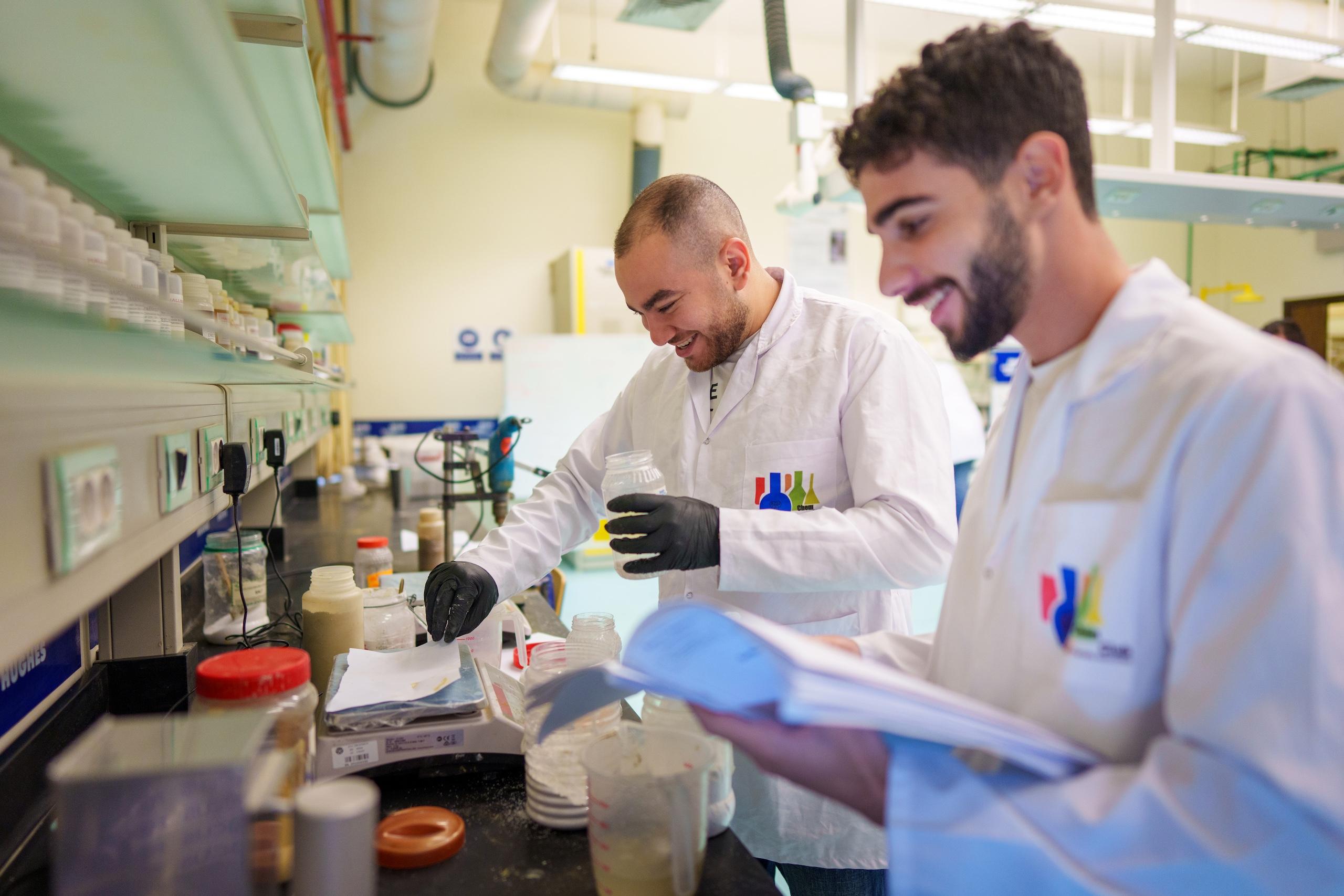 two men wearing white coats in a lab room working on an experiment
