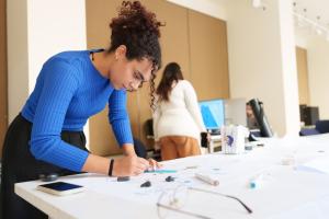 a girl with a hair bun wearing a blue shirt and drawing on a paper