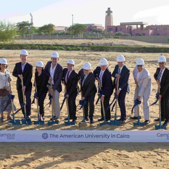 A group of men and women holding shovels on a step. Text: Campus 2026 Groundbreaking. The American University in Cairo