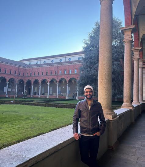 A male student is standing and smiling in front of an old building