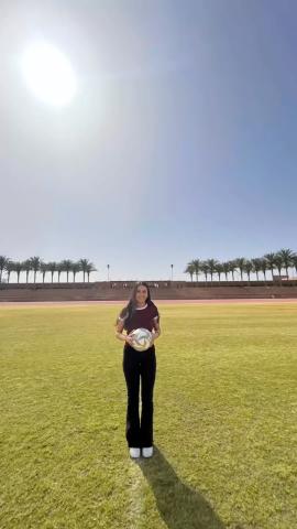 A girl is standing in a green field and holding a football