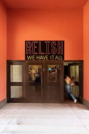 A girl entering a food outlet through a wooden door with the sign of Relish