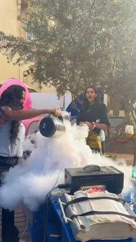 Two women surrounded by cloud of smoke as they stand near a table