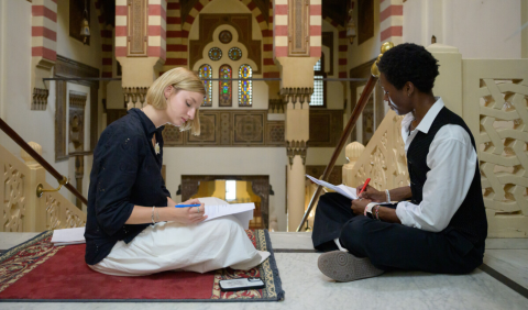 Two students sit and write at the top of a staircase