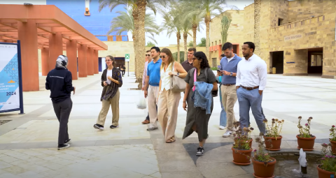 Males and females are walking on campus. They are guided by a veiled female