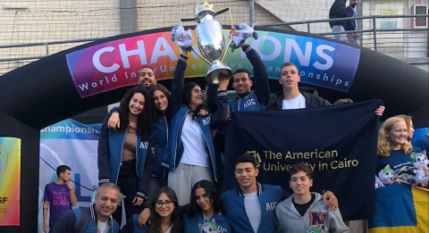 A group of athlete students holding the Egyptian flag and a silver cup