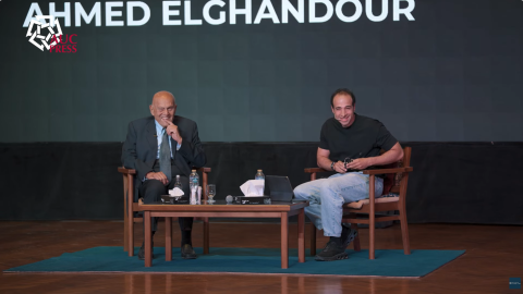 Sir Magdi Yacoub and alumni Ahmed Elghandour sitting on a stage. They are looking at the audience and smiling